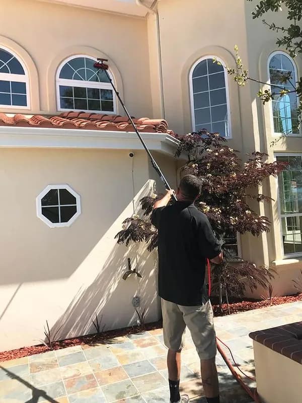 Cleaning upper story windows with a water fed pole at a stucco home
